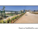 The image shows a long, empty walkway with a green fence on one side and a variety of plants and trees on the other. The walk...