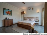 The image shows a modern and spacious bedroom with a large bed in the center. The bed has a wooden headboard and is covered w...