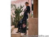 The image shows a young woman standing on a stone staircase in a tropical setting. She is wearing a long, flowing dress with...