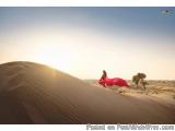 The image shows a woman in a red dress walking on a sand dune in the desert. The sky is clear and blue, and the sun is shinin...