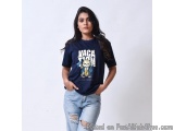 The image shows a young woman standing in front of a plain white background. She is wearing a navy blue t-shirt with a graphi...