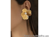 The image shows a close-up of a person's ear wearing a pair of earrings. The earrings are in the shape of a flower with a pea...