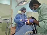 The image shows a dental clinic with two dental professionals working on a patient's teeth. The patient is lying on a dental...