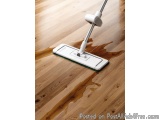 The image shows a mop on a wooden floor. The mop has a white handle and a green mop head. The floor is made of light-colored...