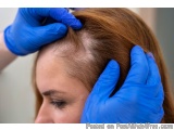The image shows a close-up of a woman's head being examined by a doctor. The doctor is wearing blue gloves and is holding the...