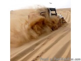 The image shows a white jeep driving through a desert-like landscape. The jeep is in the center of the image, with its front...
