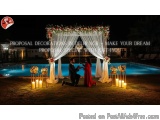The image shows a romantic scene of a couple proposing under a beautiful arch decorated with flowers and greenery. The arch i...