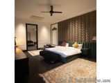 The image shows a modern and luxurious bedroom with a large bed in the center. The bed has a dark green velvet headboard and...