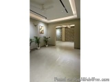 The image shows an empty room with a high ceiling and a chandelier hanging from it. The floor is made of white tiles and ther...