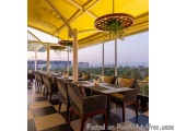 The image shows a restaurant with a beautiful view of the city. The restaurant has a large open space with a high ceiling cov...