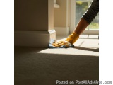The image shows a person's hand wearing yellow rubber gloves and cleaning a beige carpet. The person is holding a blue cloth...