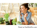 The image shows a young woman sitting at a wooden table with a bowl of salad in front of her. She is wearing a blue striped s...