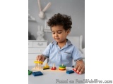 The image shows a young boy with curly hair playing with a wooden toy set. He is wearing a blue polo shirt and is sitting at...