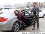 The image shows a man and a woman getting out of a silver car. The car is parked in a parking lot with other cars and buildin...