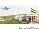 The image shows the exterior of a school building with the Indian flag flying on top. The building is orange and white in col...