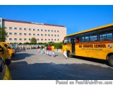 The image shows a group of students walking towards a yellow school bus. The bus has the words "Raj Vedanta School" written o...