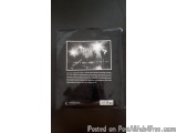 The image is a black and white photograph of a group of people standing on a stage with their arms raised in the air. The sta...