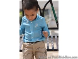 The image shows a young boy, probably around 2-3 years old, standing on a black metal bench. He is wearing a light blue butto...