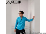 The image shows a young man wearing a blue shirt with small white polka dots on it. He is standing in front of a white wall w...