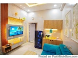 The image shows a modern living room with a blue sofa on the right side and a wooden entertainment center on the left side. T...