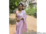 The image shows a young woman standing on a dirt road in an Indian village. She is wearing a traditional Indian saree in a li...