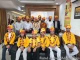 The image shows a group of people posing for a group photo in a room. There are nine people in the photo, all wearing traditi...
