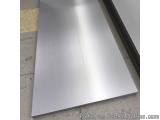 The image shows a long, rectangular metal sheet lying on a concrete floor. The sheet appears to be made of stainless steel an...