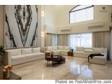 The image shows a modern living room with a large white sofa set in the center. The sofa set has a modern design with a curve...