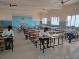 The image shows a classroom with rows of desks and chairs arranged in neat rows. There are three students sitting at the desk...