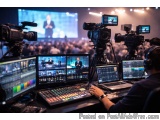 The image shows a large conference room with multiple video and audio equipment. There are multiple monitors and laptops on t...