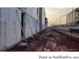 The image shows a construction site with a long, narrow dirt path leading up to a building on the left side. The building app...