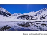 The image is a landscape photograph of a mountain range with a lake in the foreground. The mountains are covered in snow and...
