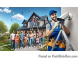 The image shows a group of people standing in front of a house. The house is a two-story building with a sloping roof and a c...