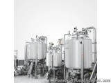 The image shows a group of large stainless steel tanks in a factory or industrial setting. The tanks are cylindrical in shape...