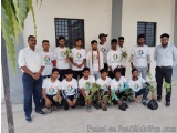 The image shows a group of young men posing for a group photo in front of a building. They are all wearing white t-shirts wit...