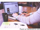 The image shows a person sitting at a wooden desk with a laptop in front of them. The laptop screen displays a website with a...