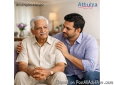 The image shows an elderly man sitting on a couch with a younger man sitting next to him. The elderly man is wearing a beige...