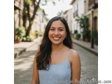 The image is a portrait of a young woman standing on a cobblestone street. She is smiling and looking directly at the camera....