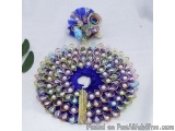 The image is of a peacock-shaped brooch. The brooch is made up of multiple layers of blue and purple fabric, with the blue fa...