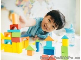 The image shows a young boy playing with colorful building blocks on a white table. He is wearing a blue shirt and has a big...