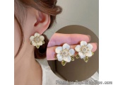 The image shows a close-up of a woman's ear wearing a pair of earrings. The earrings are in the shape of a flower with five p...