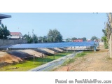 The image shows a large solar panel installation in a rural area. The panels are arranged in a grid-like pattern and are supp...
