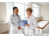 The image shows two women in white lab coats standing in a hospital room. The woman on the left is a young female doctor with...