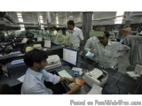 The image shows a large office space with multiple desks and computers. There are several people working on the desks, some o...