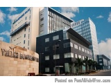 The image shows a modern office building with a blue sky and clouds in the background. The building is located in a city with...