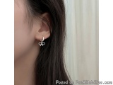 The image shows a close-up of a person's ear. The person has long dark hair and is wearing a pair of silver earrings. The ear...