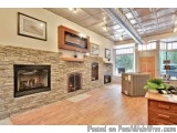 The image shows a modern living room with a large stone fireplace in the center. The fireplace is made of stacked stone and h...