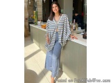 The image shows a young woman standing in front of a bar counter in a restaurant or bar. She is wearing a blue and white stri...