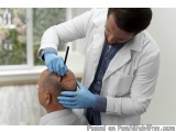 The image shows a doctor in a white lab coat and blue gloves examining a patient's head. The doctor is standing behind the pa...