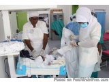 The image shows a group of medical professionals in a hospital room. There are three women in the image, all wearing white un...
